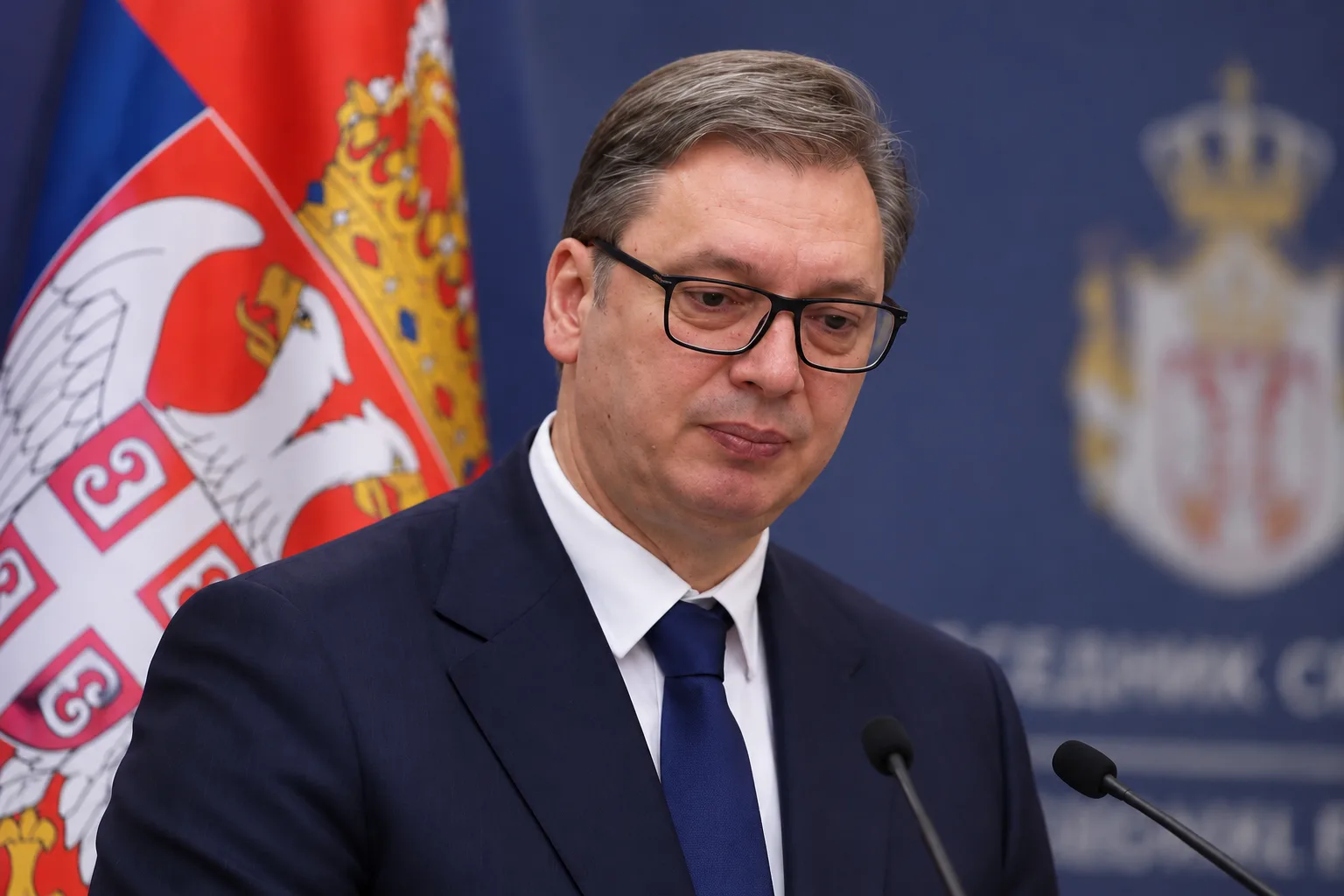 Serbiens Präsident Aleksandar Vučić mit ernstem Gesichtsausdruck bei einer Pressekonferenz vor serbischer Flagge und Regierungshintergrund.